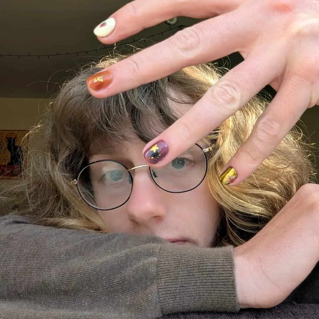 Connor Ridley shows their painted nails to the camera, slightly covering their face.