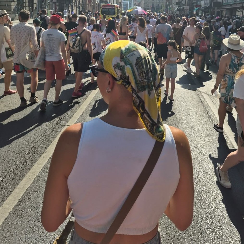 Photo of Maple Saffron Nagy, project manager at queer web design, at Budapest pride, back turned to the camera in the midst of a crowd of people.